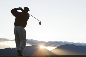 A golfer teeing off at sunrise.