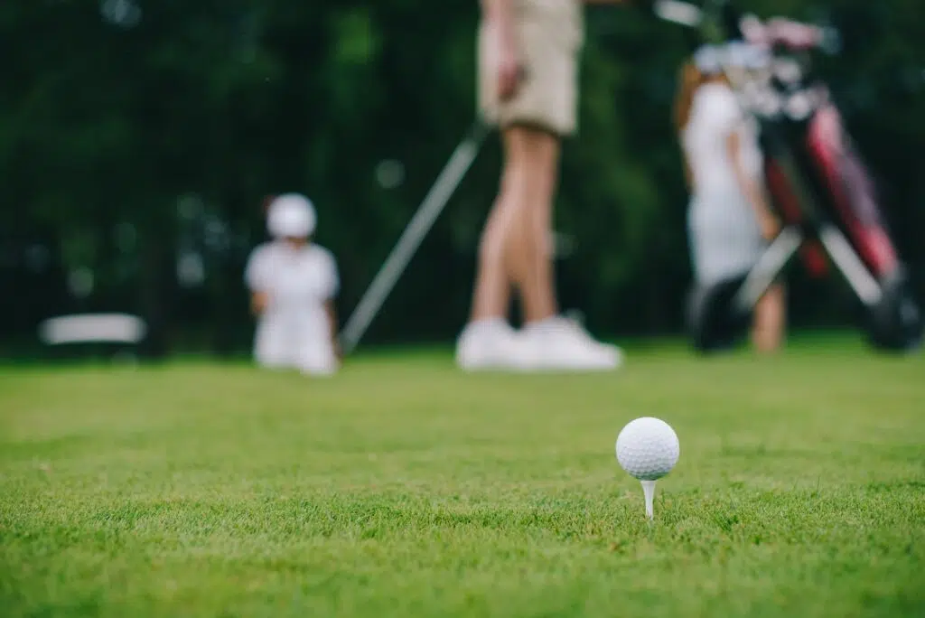 selective focus of golf ball on green lawn and golf players behind