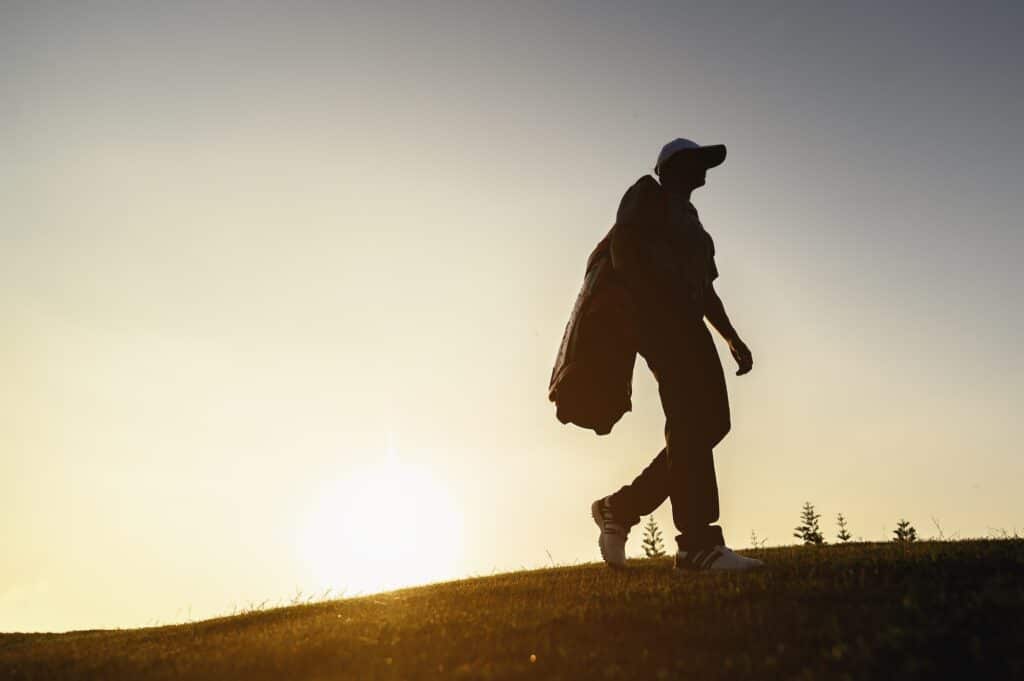A man is carrying a golf bag on a hill at a golf course to practice golfing skills professionally.