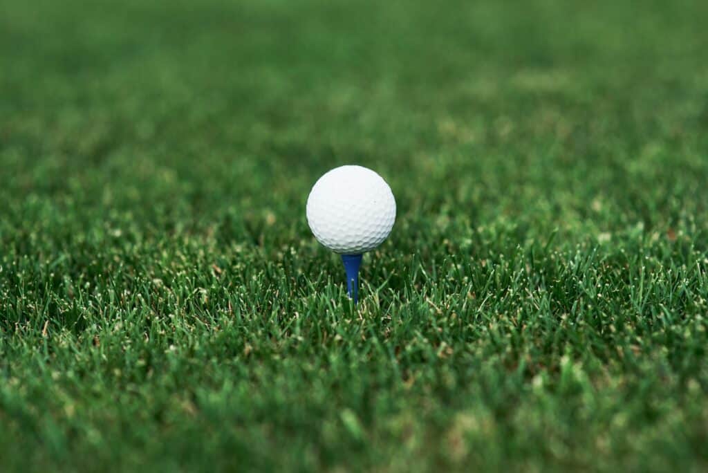 Close up photo of golf ball standing on the pin in the green lawn