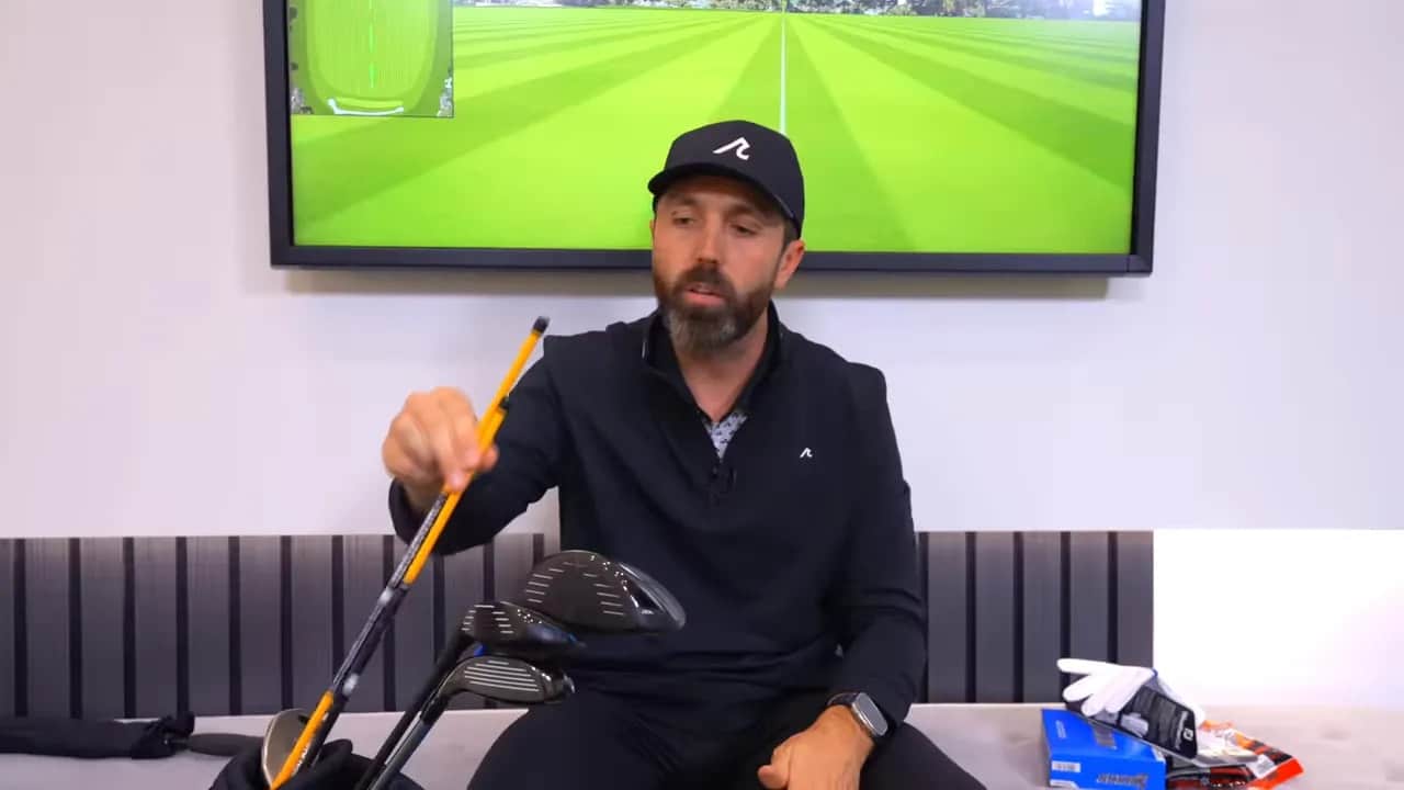 Moderator zeigt Alignment‑Sticks im Golfbag; Handschuhe und Ballbox liegen rechts